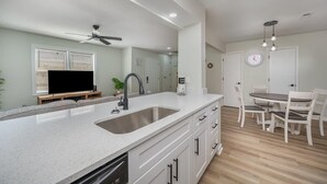 Een moderne keuken met een groot eiland, witte kasten, een ingebouwde vaatwasser en een eethoek met een tafel en stoelen.