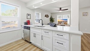 Une cuisine moderne avec des meubles blancs, un lave-vaisselle, un évier et un ventilateur de plafond.