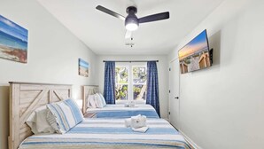 Une chambre à coucher avec un lit, un ventilateur de plafond, une fenêtre avec des rideaux et un téléviseur fixé au mur.