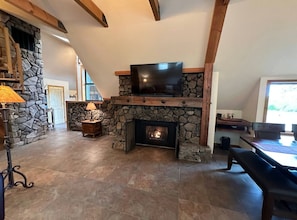 A stone fireplace with a TV above it, a stone wall, and a wooden ceiling. - Riverfront Retreat w/ hot tub minutes to Sunriver (Sunriver)
