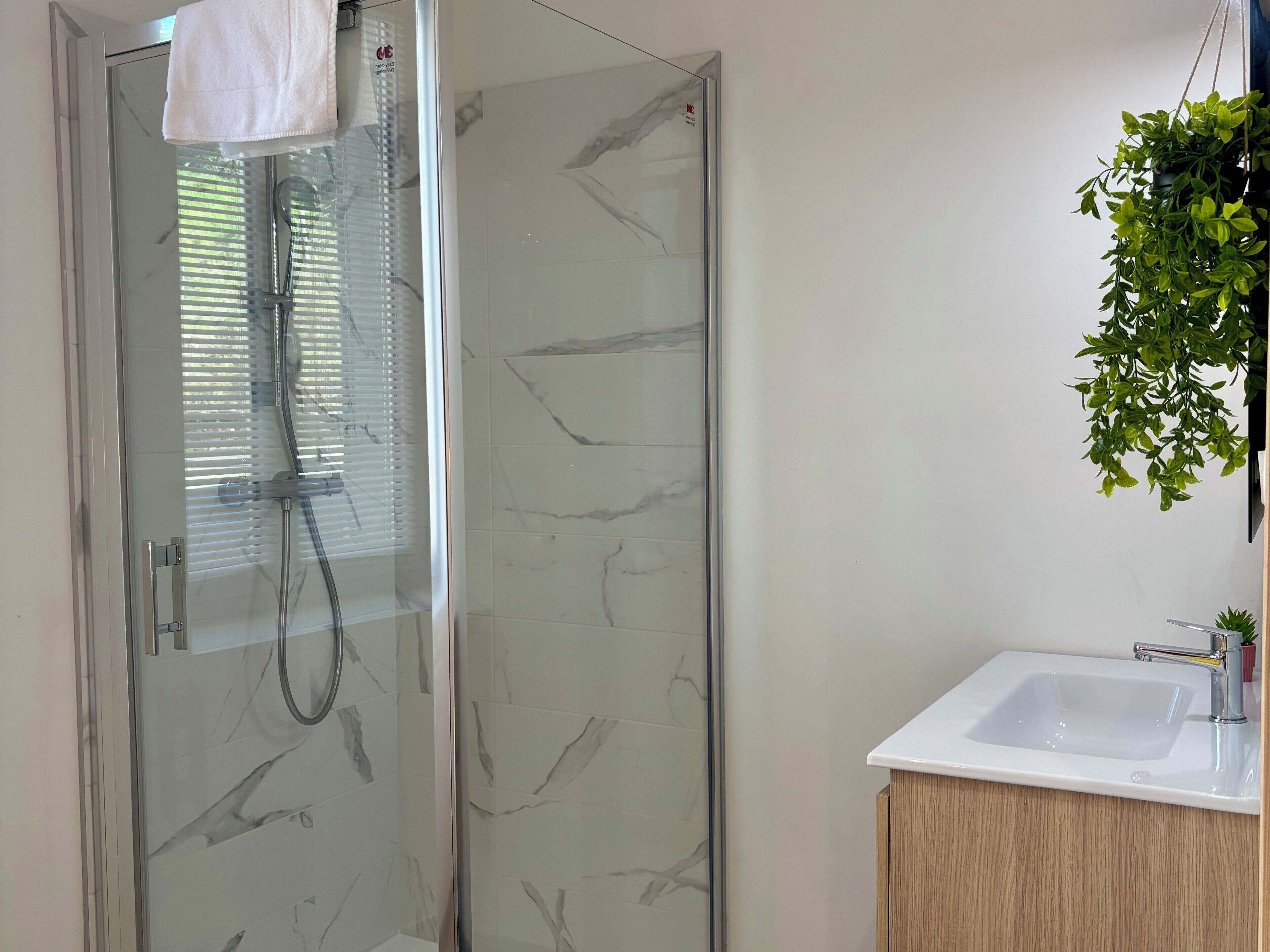 A modern bathroom with a glass shower enclosure, a white sink, and a wooden cabinet.