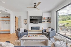 Un salon moderne doté d’une cheminée, de deux canapés, d’une table basse et d’une grande fenêtre donnant sur l’extérieur.