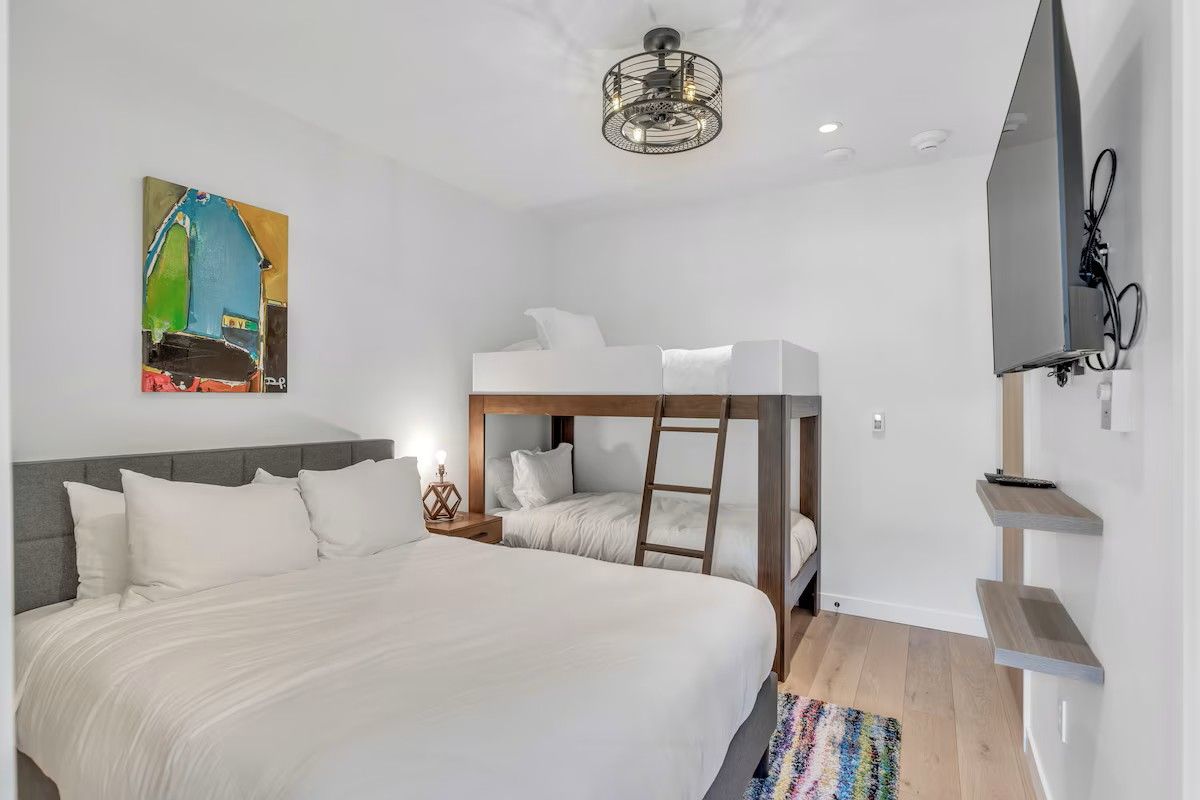 Une chambre avec un lit superposé, un grand lit, un tableau, un luminaire au plafond et un téléviseur fixé au mur.