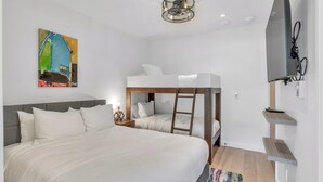 Een slaapkamer met een stapelbed, een groot bed, een schilderij, een plafondlamp en een aan de muur bevestigde televisie.