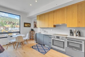 A modern kitchen with wooden cabinets, a large window, and a dining area with white chairs.