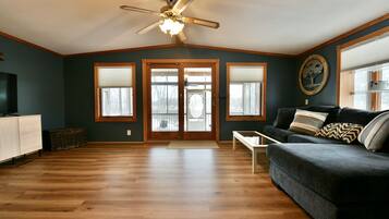 Ein geräumiges Wohnzimmer mit dunkelblauer Wand, Deckenventilator, dunkelblauem Sofa und Holzboden.