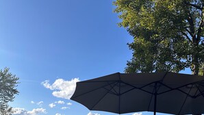 Una tienda de campaña, un paraguas y un árbol en una zona arenosa con cielo despejado.