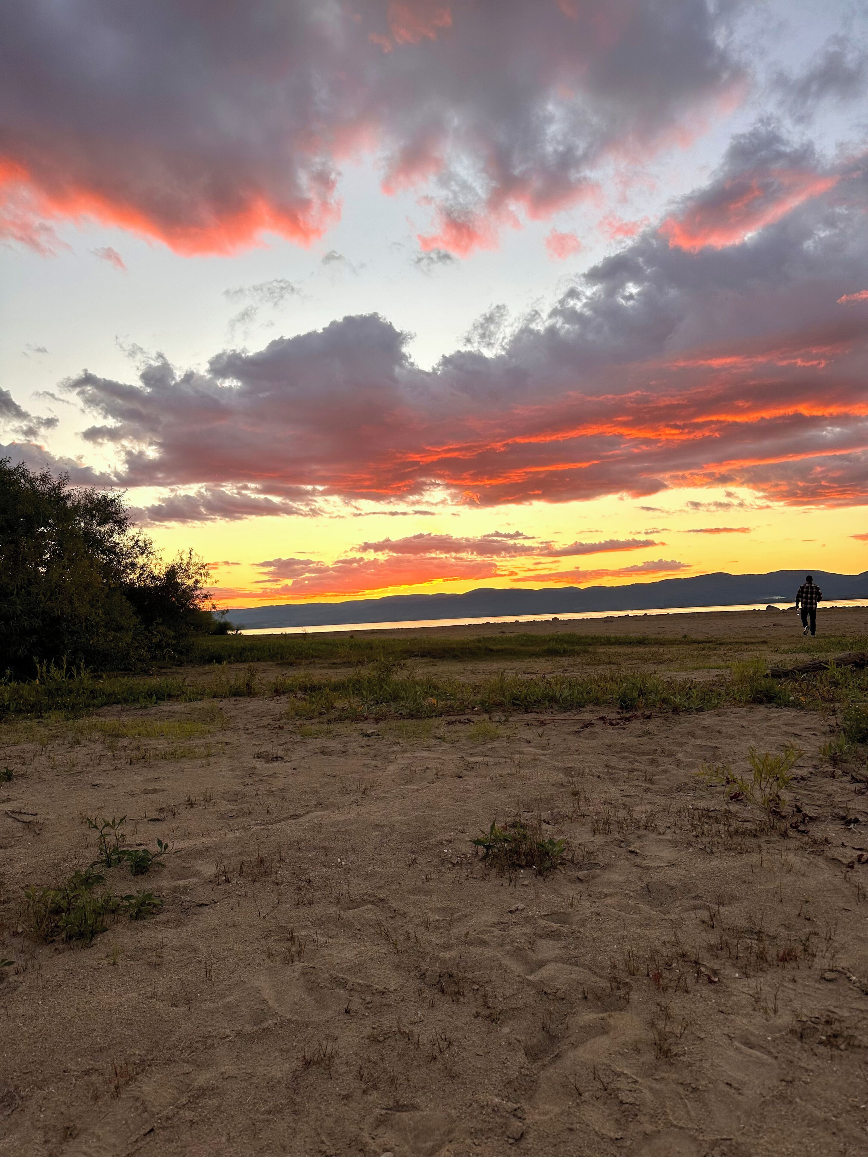 A wide, open field with a person walking towards a sunset.