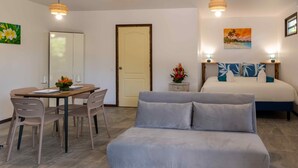 Ein Zimmer mit einem Bett, einem Sofa, einem Esstisch mit Stühlen, einem kleinen Beistelltisch mit einer Vase und einer Tür.