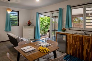 A dining area with a table set for two, a refrigerator, and a sliding glass door leading to a garden.
