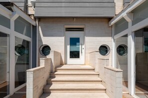 La entrada de un edificio con una escalinata que lleva a una puerta, flanqueada por puertas de cristal con ventanas circulares.
