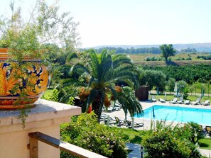 Ein Poolbereich mit Liegestühlen und Palmen, umgeben von viel Grün und einem Zierteich.