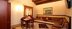 A living room with a sofa, a dining table with chairs, a rug, and a painting on the wall. - Agriturismo Badiula (Carlentini)