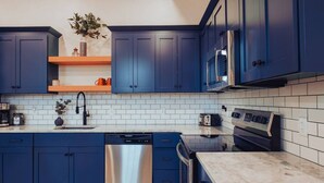 A modern kitchen with blue cabinets, a stainless steel dishwasher, a built-in oven, and a microwave. - American Hall Young Suite (Millersburg)