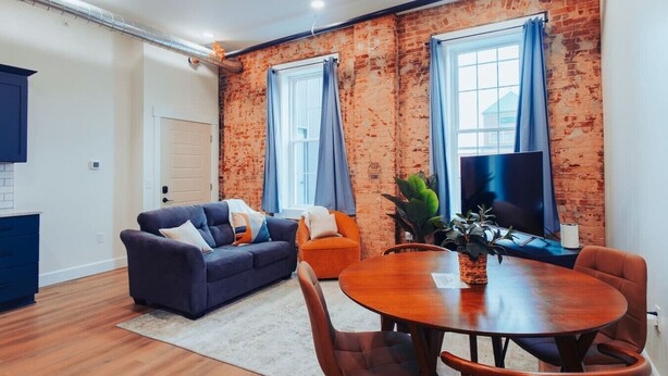A modern living room with a sofa, a dining table, and a TV. - American Hall Young Suite (Millersburg)