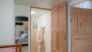Ein Zimmer mit einem Bett, einer Holzleiter, einem Kleiderschrank und einem Spiegel, der ein anderes Zimmer reflektiert.