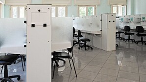 Ein großzügiger Arbeitsbereich mit einzelnen Arbeitsplätzen, jeweils durch eine Trennwand abgegrenzt, schwarzen Bürostühlen und einem Fliesenboden.