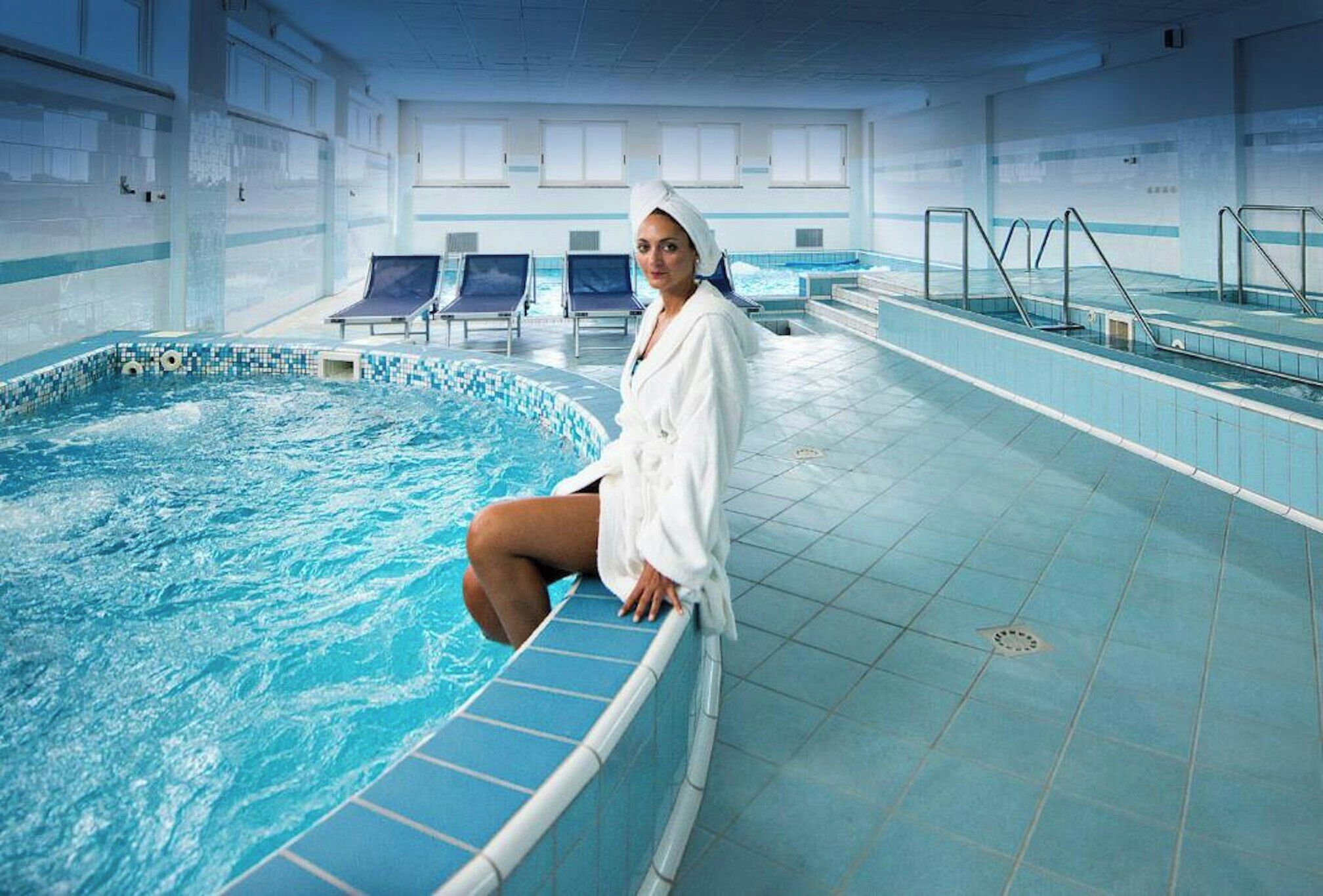 Una persona sentada junto a una piscina con paredes y piso de baldosas.