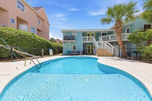A swimming pool with a metal ladder, a palm tree, and a two-story building with balconies. - Wavecrest Grand with Pool Great for Groups (Surfside Beach)