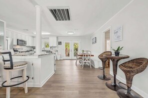 A modern kitchen with white cabinetry, a central island, and a dining area with wicker chairs and a small table. - Wavecrest Grand with Pool Great for Groups (Surfside Beach)