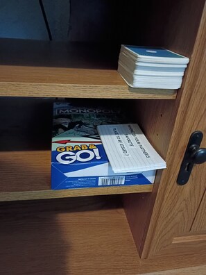 A wooden cabinet with a Monopoly board game and a stack of cards on top.