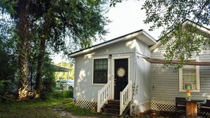 A small, single-story house with a front porch, a mailbox, and a wooden table with chairs. - THE JAX HIDEOUT 
DT studio w/shaded patio (Jacksonville)