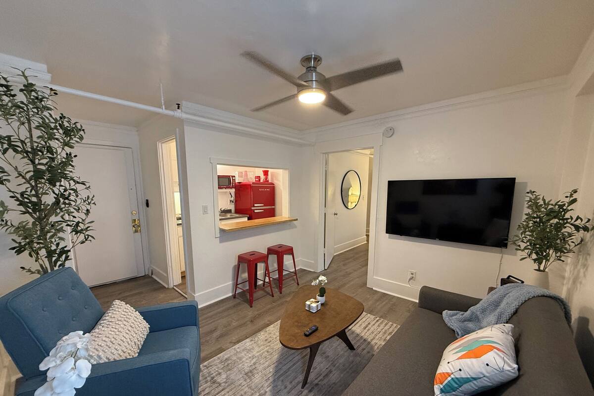 A living room with a sofa, a coffee table, a TV, and a kitchen area with red appliances.