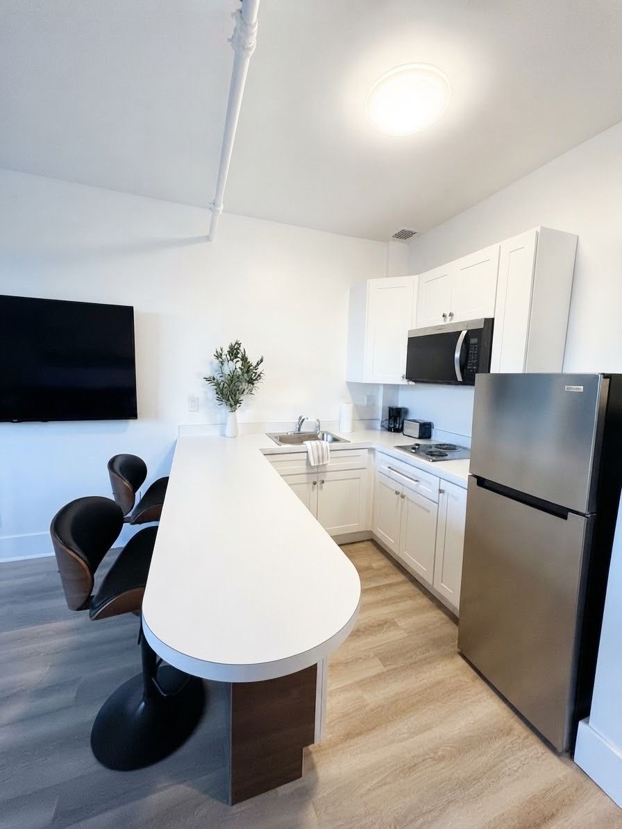 Una cocina moderna con encimera blanca, electrodomésticos de acero inoxidable y un comedor con sillas.