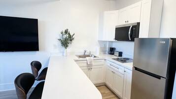 Una cocina moderna con encimera blanca, electrodomésticos de acero inoxidable y un comedor con sillas.