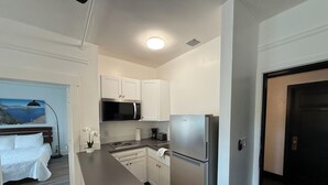 A compact kitchen with white cabinets, a stainless steel refrigerator, a microwave, and a small countertop. - The Historic George Hotel (Klamath Falls)