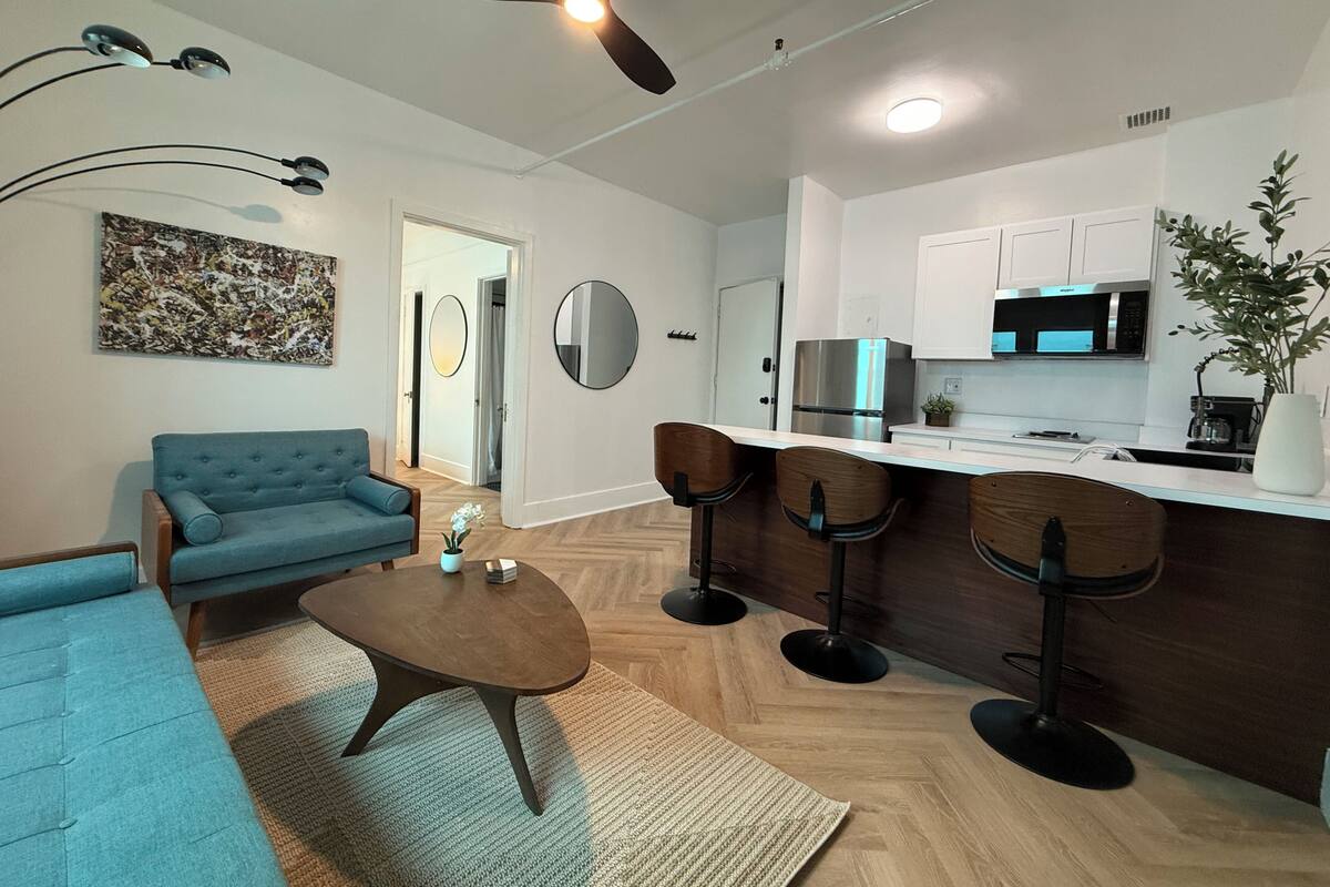 A modern living room with a sofa, coffee table, and a dining area with bar stools.