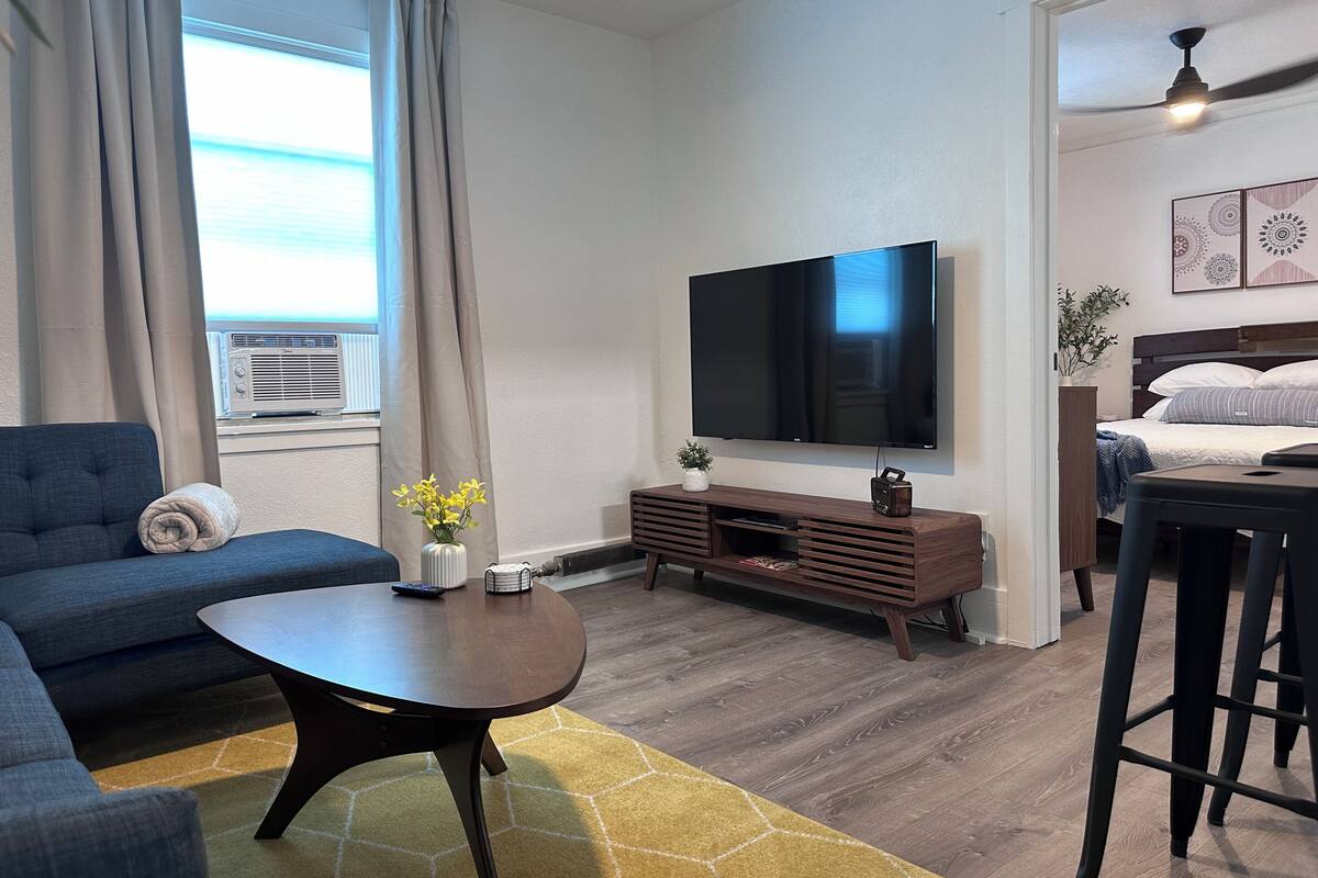 A modern living room with a sofa, a coffee table, a TV, and a bed.