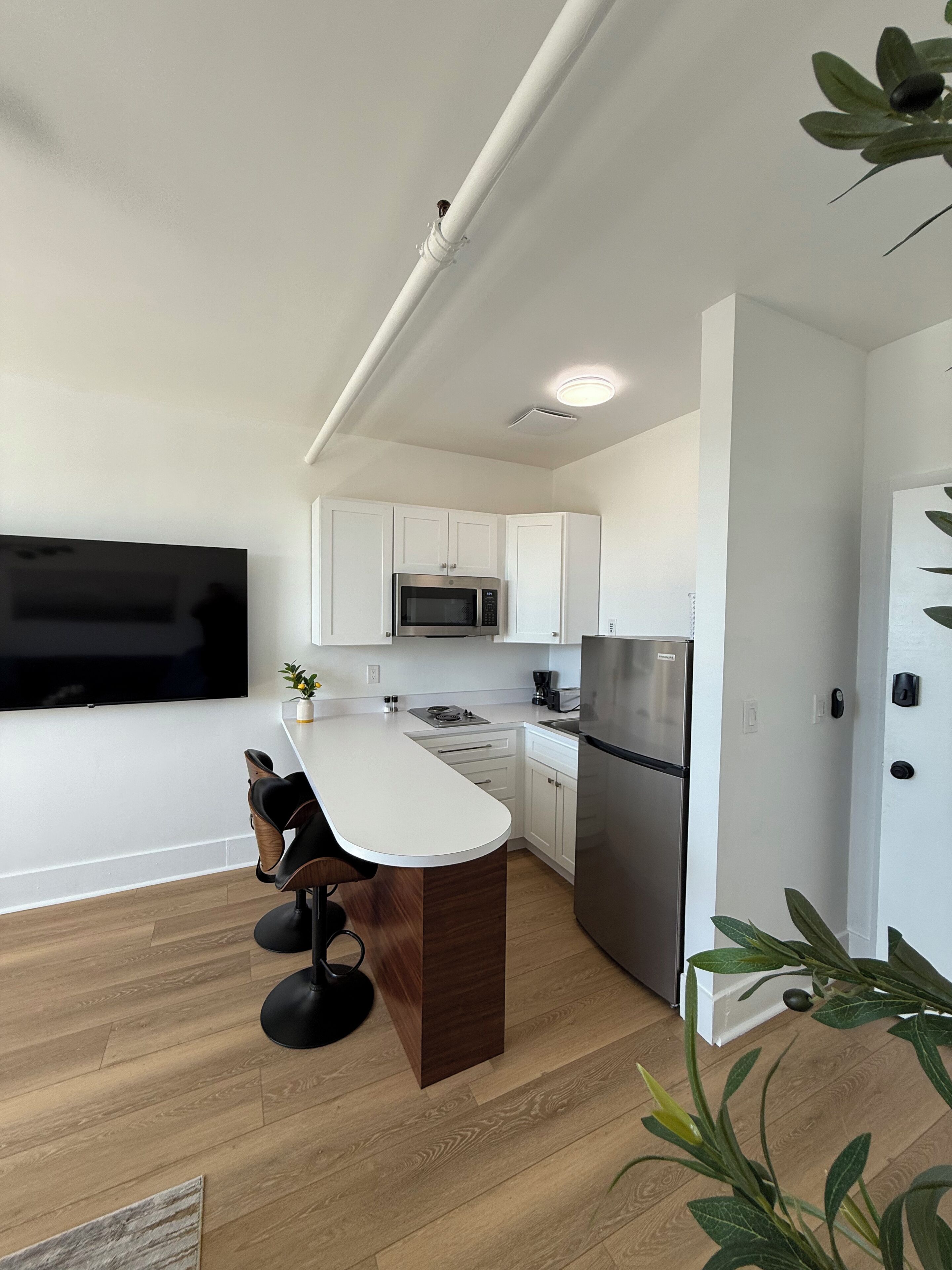 A modern kitchen with white cabinets, a stainless steel refrigerator, a microwave, and a bar area with stools.