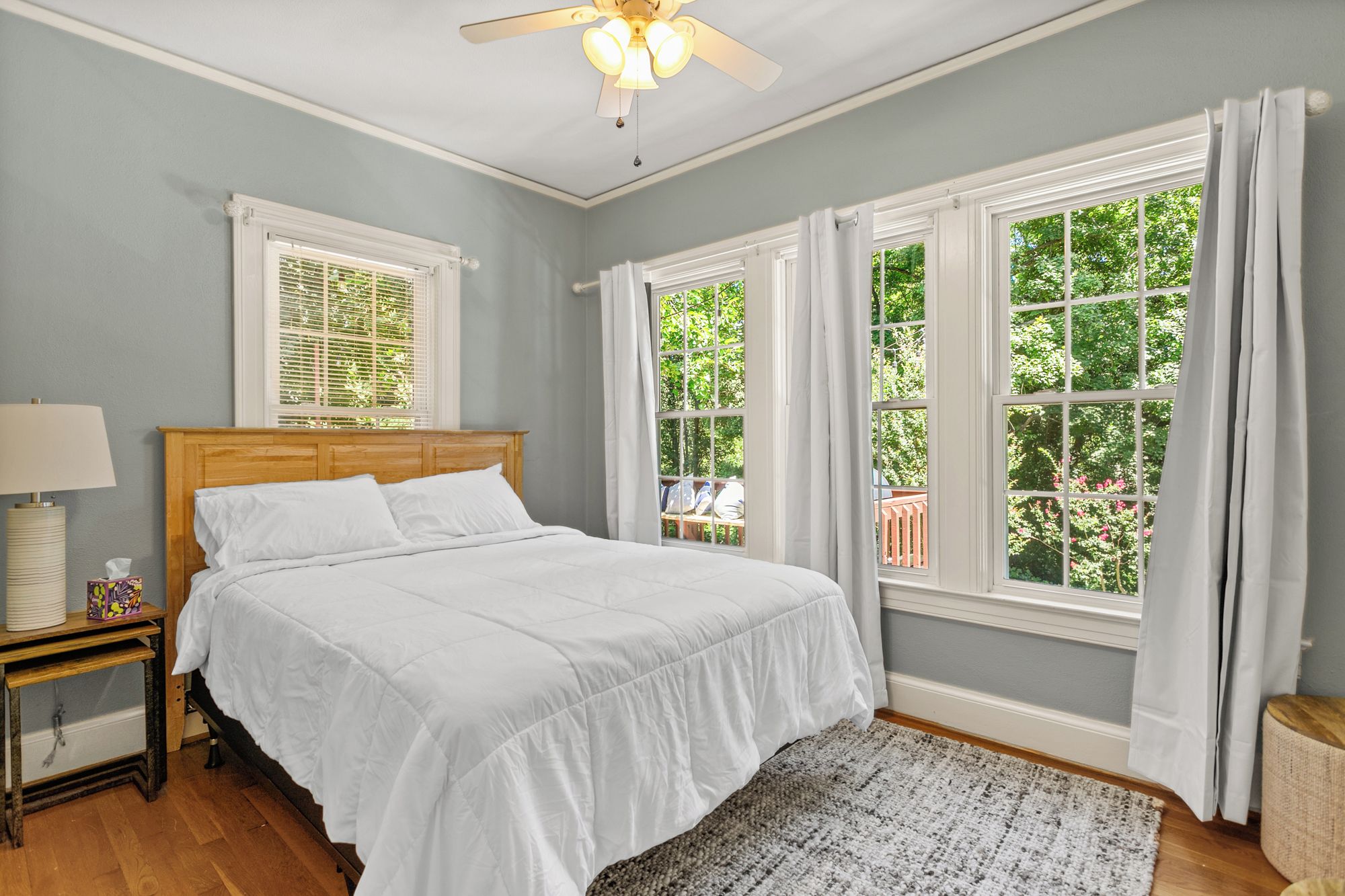 A bedroom with a bed, nightstand, lamp, and large windows with curtains.
