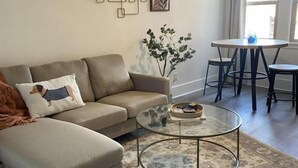 A living room with a sofa, a glass coffee table, a rug, and a dining area with a table and chairs. - The Historic George Hotel (Klamath Falls)