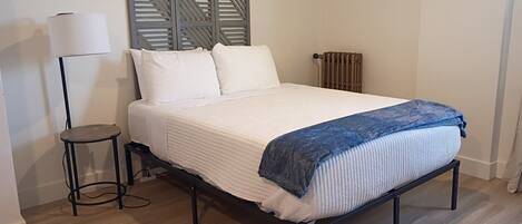 A bed with a headboard, a bedside table, a lamp, and a radiator.