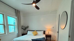 A bedroom with a bed, a ceiling fan, a bedside table, a lamp, a window, and a door. - The Historic George Hotel (Klamath Falls)