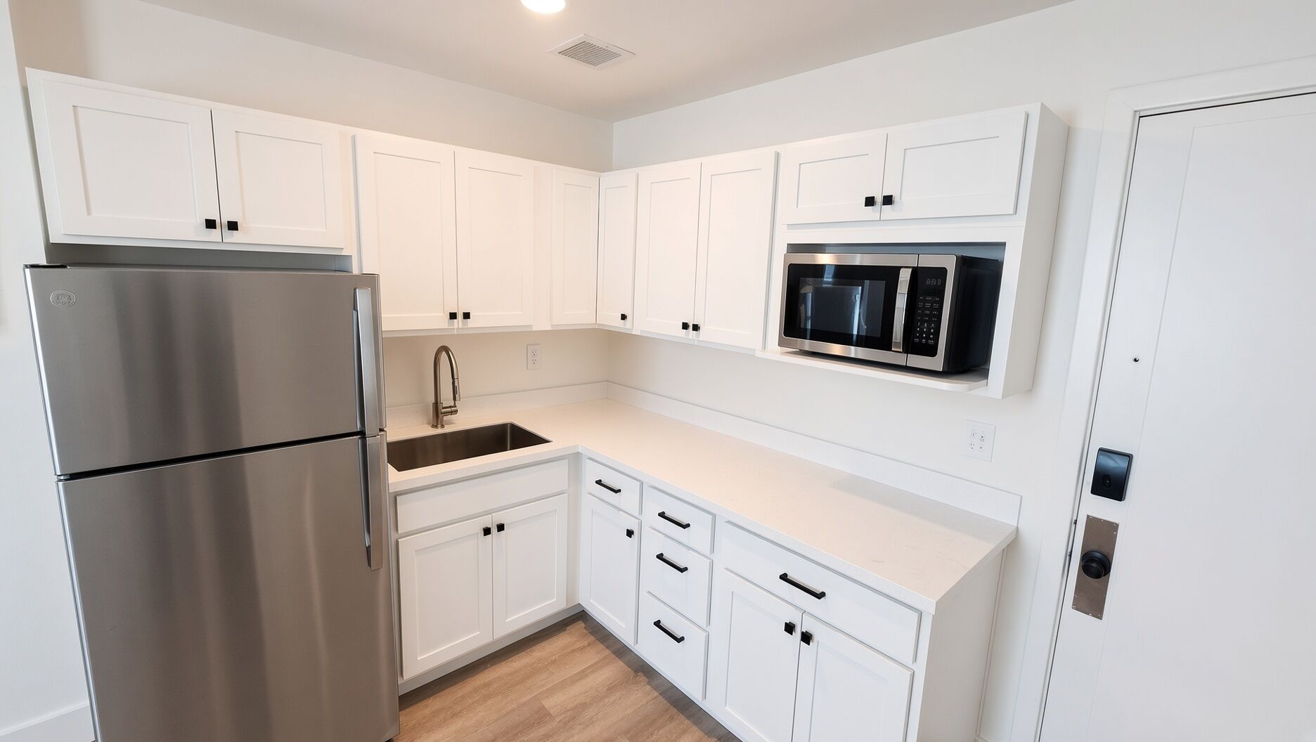 A modern kitchen with white cabinetry, a stainless steel refrigerator, a built-in microwave, and a sink.