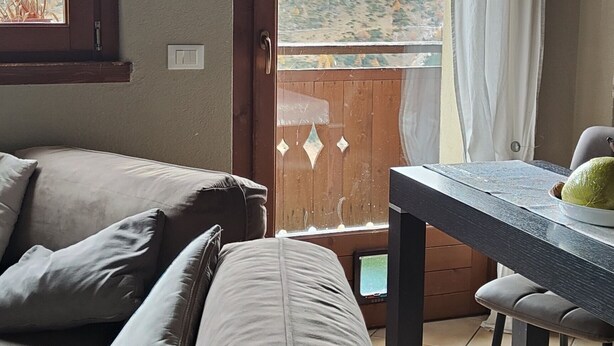 A cozy room with a sofa, a table with a plate, and a view of a mountainous landscape through a window.