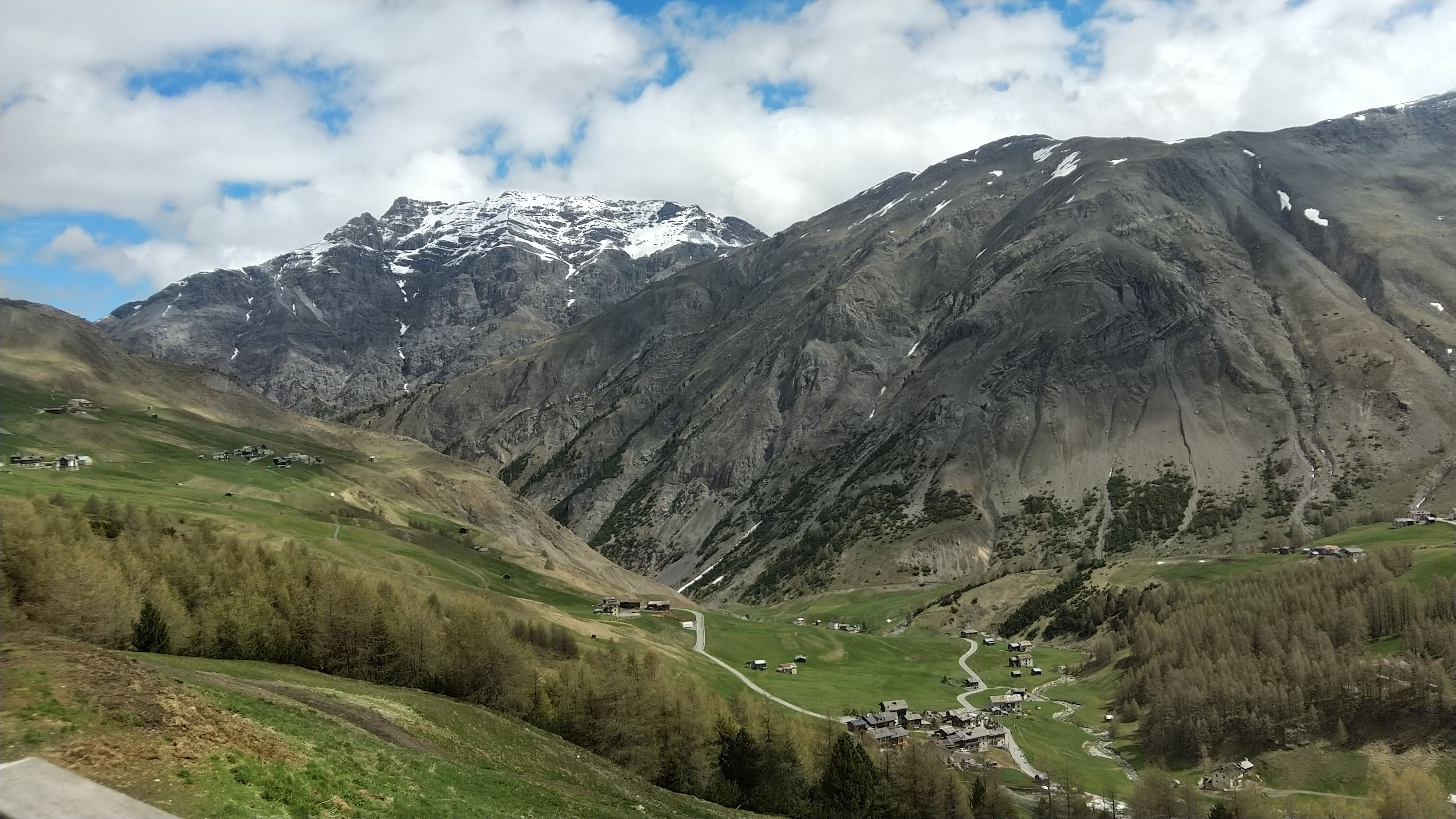 Un paisaje montañoso con un valle, una carretera serpenteante y edificios dispersos.