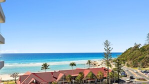 Vista sulla costa con spiaggia, cielo azzurro limpido e edifici dai tetti rossi.