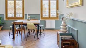 A dining area with a table and chairs, large windows, a radiator, and a bookshelf with magazines. - Raf & Liza, sublime F2 proche Vieux-Marché (Rouen)
