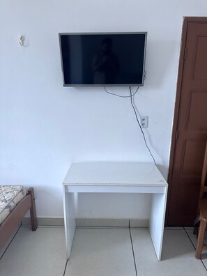 A room with a white desk, a television mounted on the wall, and a wooden door. - Hotel Ideal (Boa Vista)