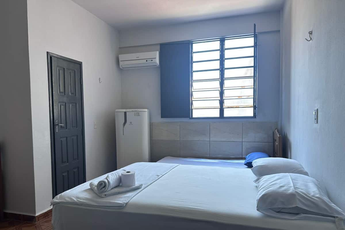 Una habitación pequeña y limpia con cama, armario, ventana con persianas y equipo de aire acondicionado.