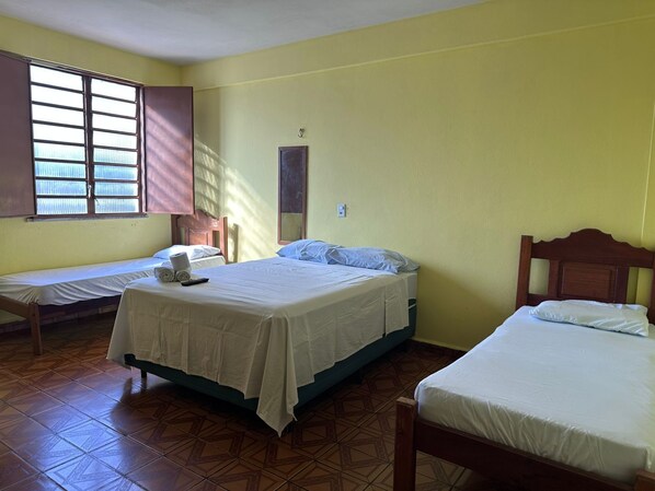 A room with three beds, a window with bars, a wall-mounted light, and a tiled floor. - Hotel Ideal (Boa Vista)