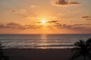 A beach scene with the sun setting over the ocean, palm trees, and people on the sand. - Apartment Beachfront view. (Puerto Escondido)