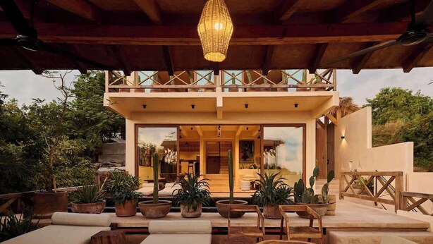 Una villa moderna con un balcone, area salotto esterna e piante in vaso.
