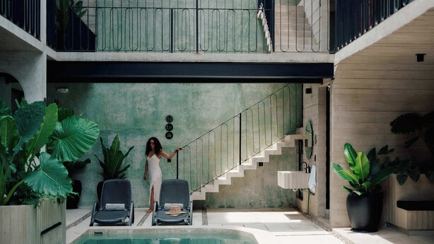 An indoor swimming pool with two lounge chairs, a staircase, and potted plants.