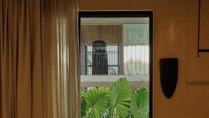 A room with a large window, beige curtains, a woven basket, and a concrete floor.