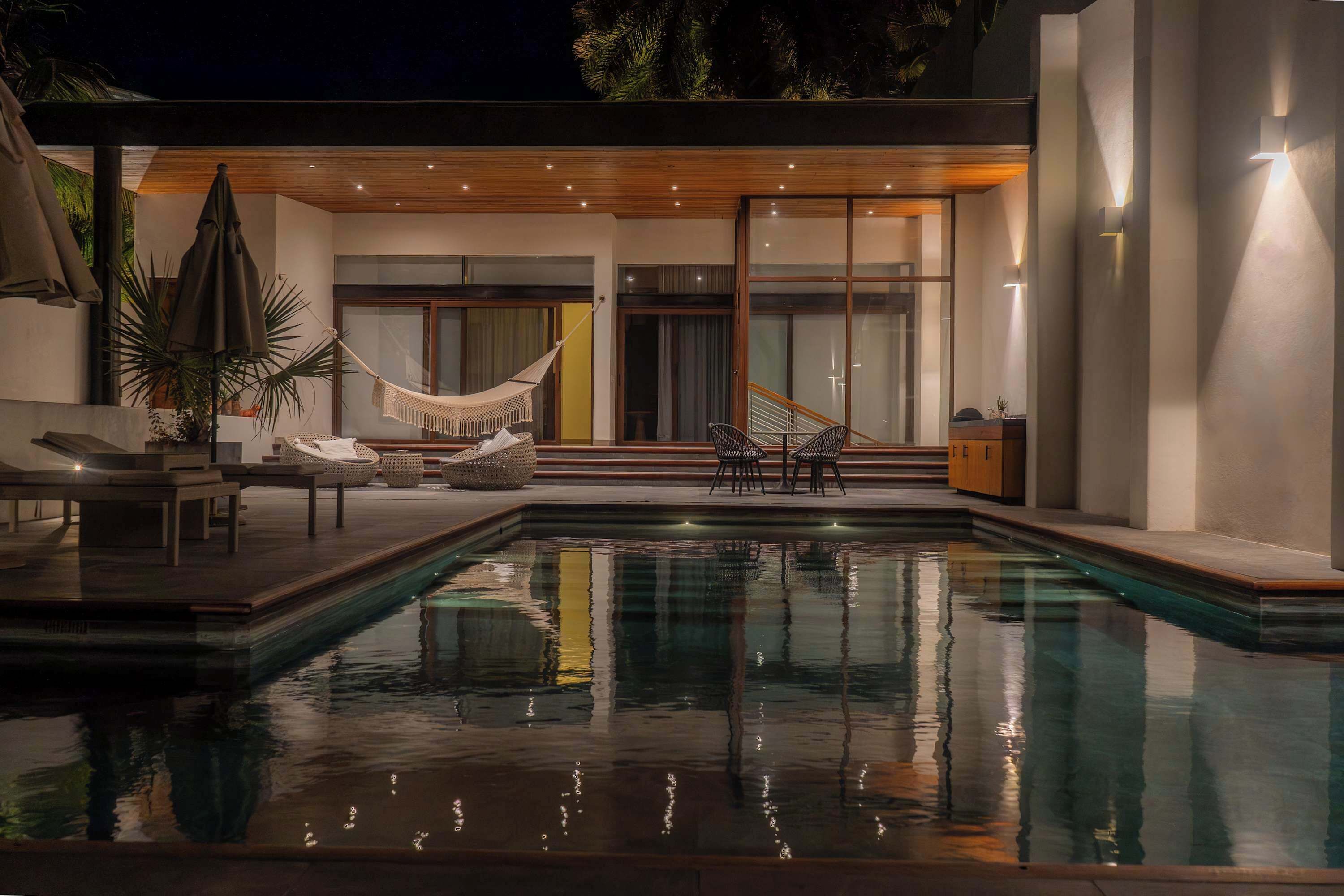 A modern outdoor pool area with a hammock, lounge chairs, and a staircase leading to a covered deck.
